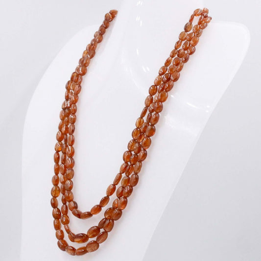 Natural Hessonite Necklace displayed with three strands of polished oval beads in whiskey color.