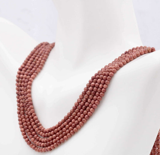 Natural Goldstone Beads strand in brownish orange color displayed on a mannequin bust, showcasing its round opaque beads.