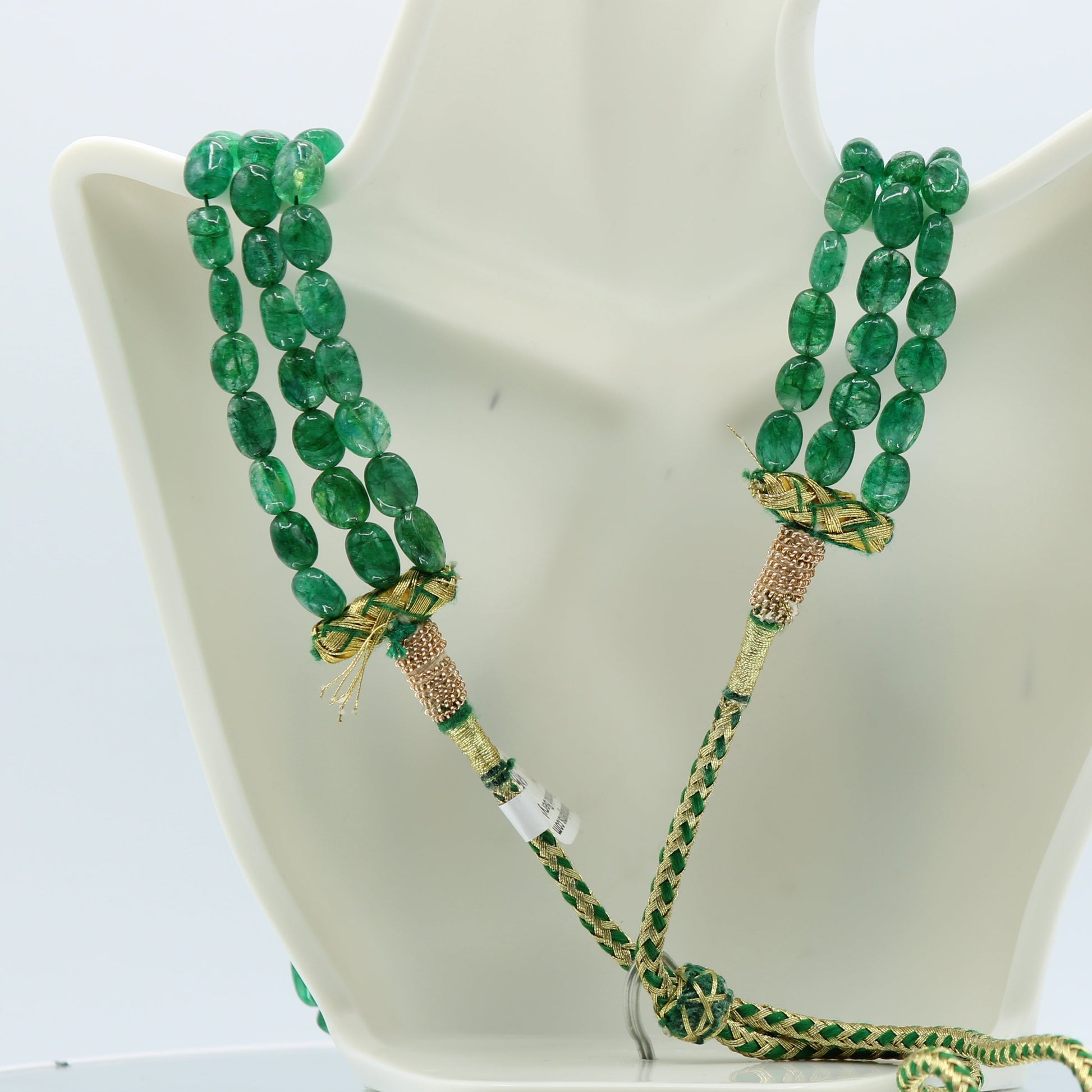 Emerald Oval Beaded Necklace displayed on a bust, showcasing three strands of polished emerald beads in green.