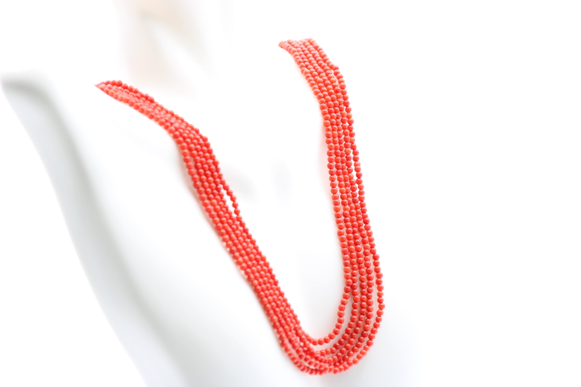 5 strand coral necklace featuring polished reddish orange coral beads on a display