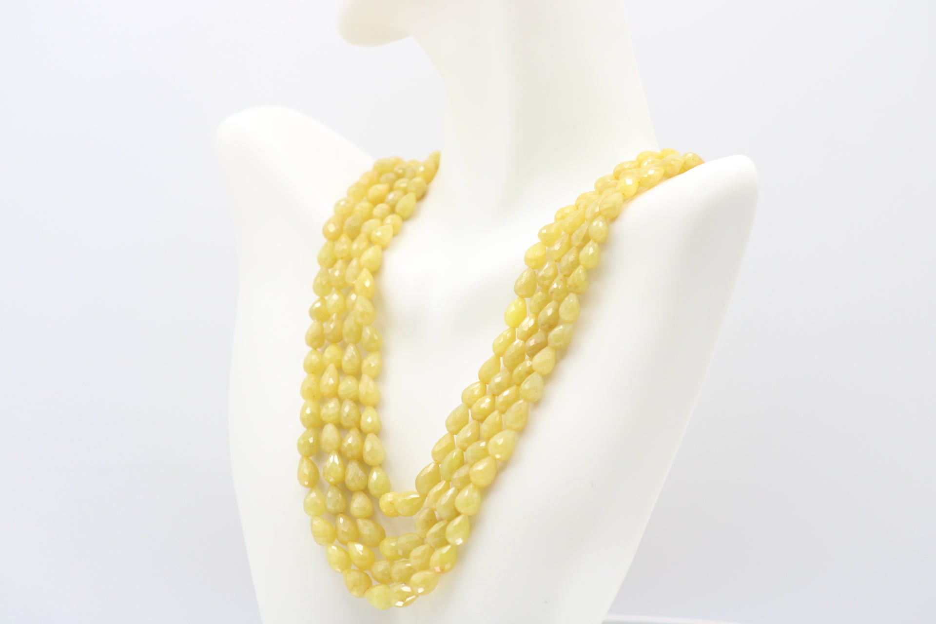 The Yellow Sapphire Briolette Pearl Shaped Necklace displayed on a bust with layered yellow sapphire beads.