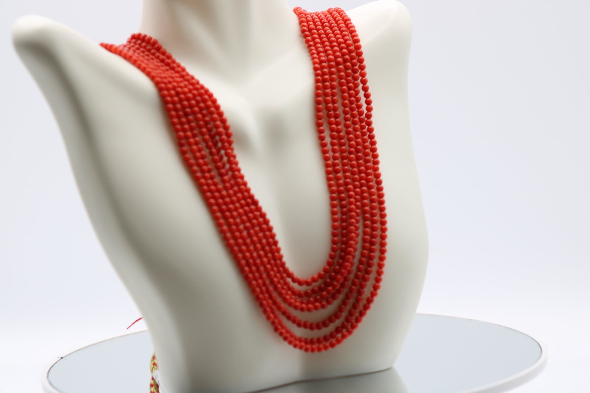 Coral Necklace 3mm - 7 Strands displayed on a bust, showcasing its reddish-orange hues and polished finish.