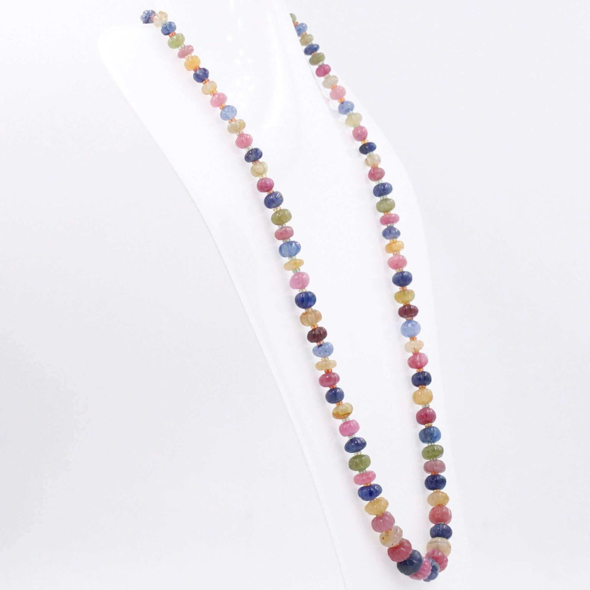 Multi-colored sapphire ruby necklace displayed on a stand, showcasing its vibrant gemstone colors and carved shapes.