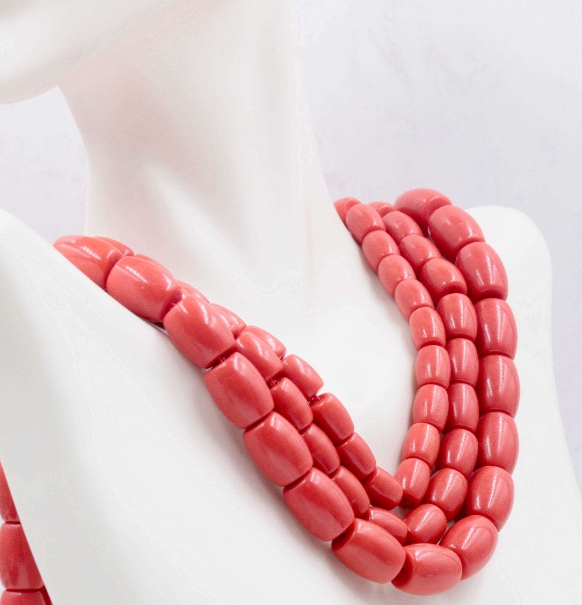 Natural coral beads strand in reddish orange color displayed elegantly on a mannequin.