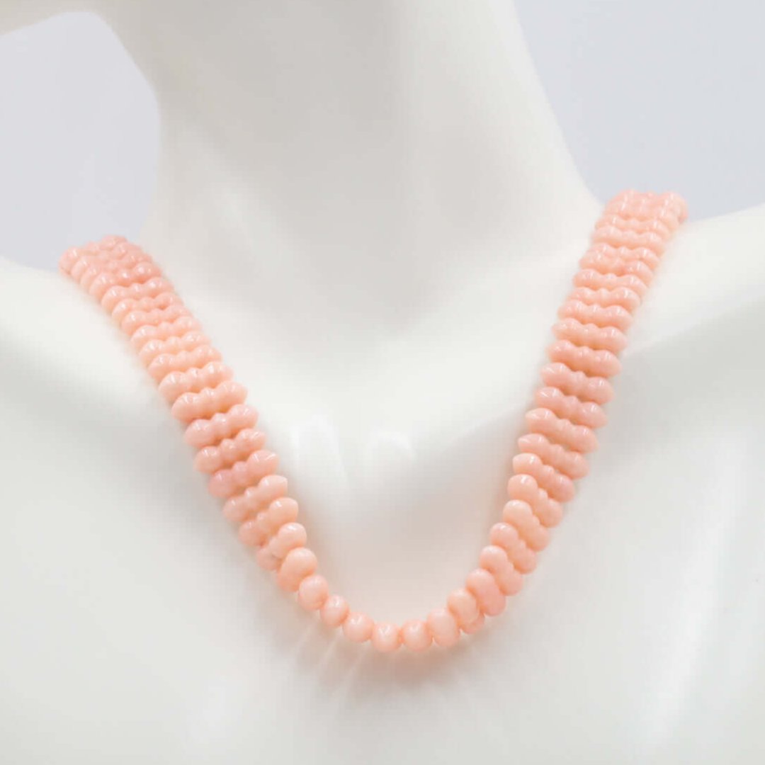 Natural coral beaded necklace in light peachy pink on display, showcasing organic gemstone beauty.