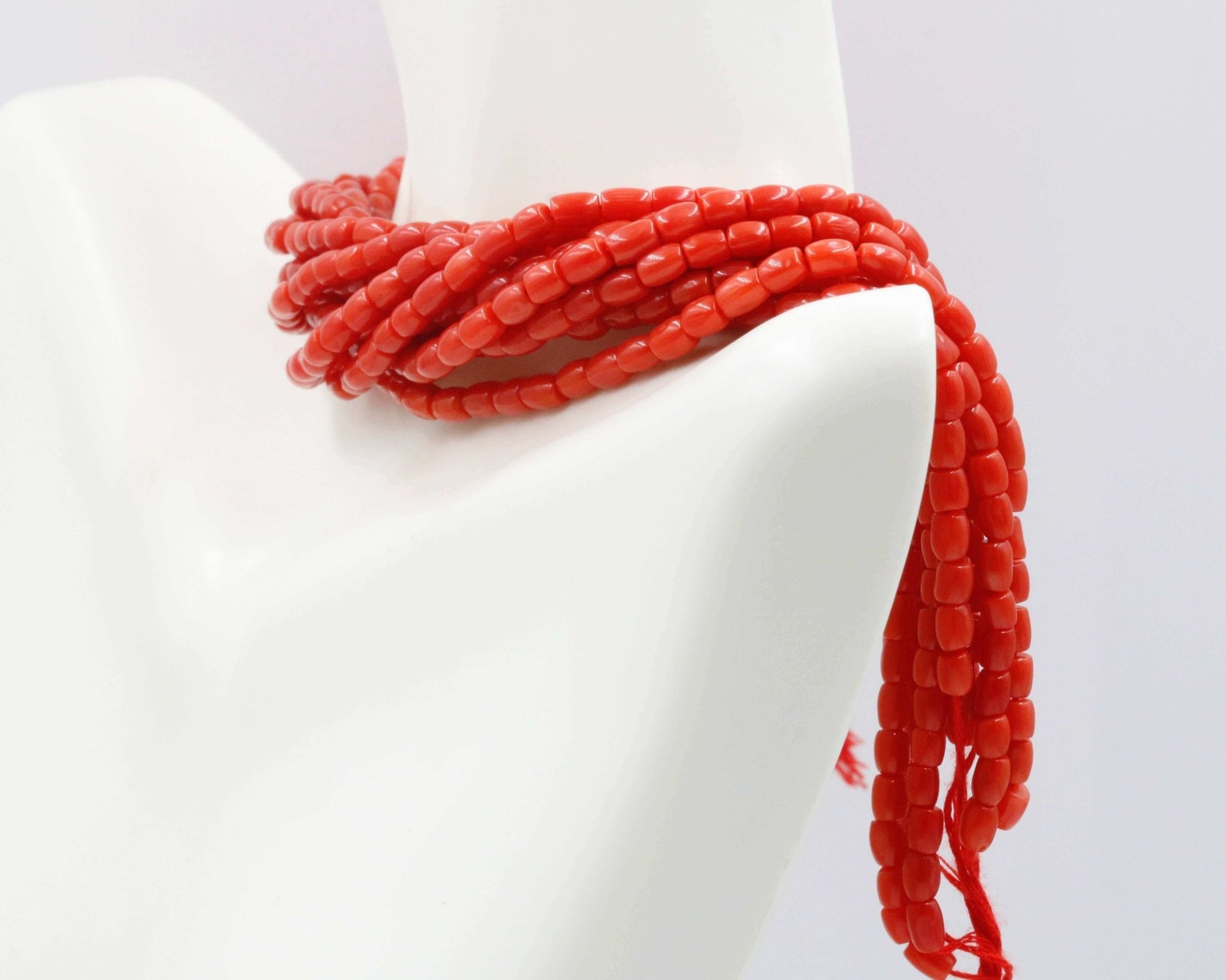 Italian Red Coral Beads Strands elegantly draped over a mannequin's shoulder, showcasing vibrant red color.