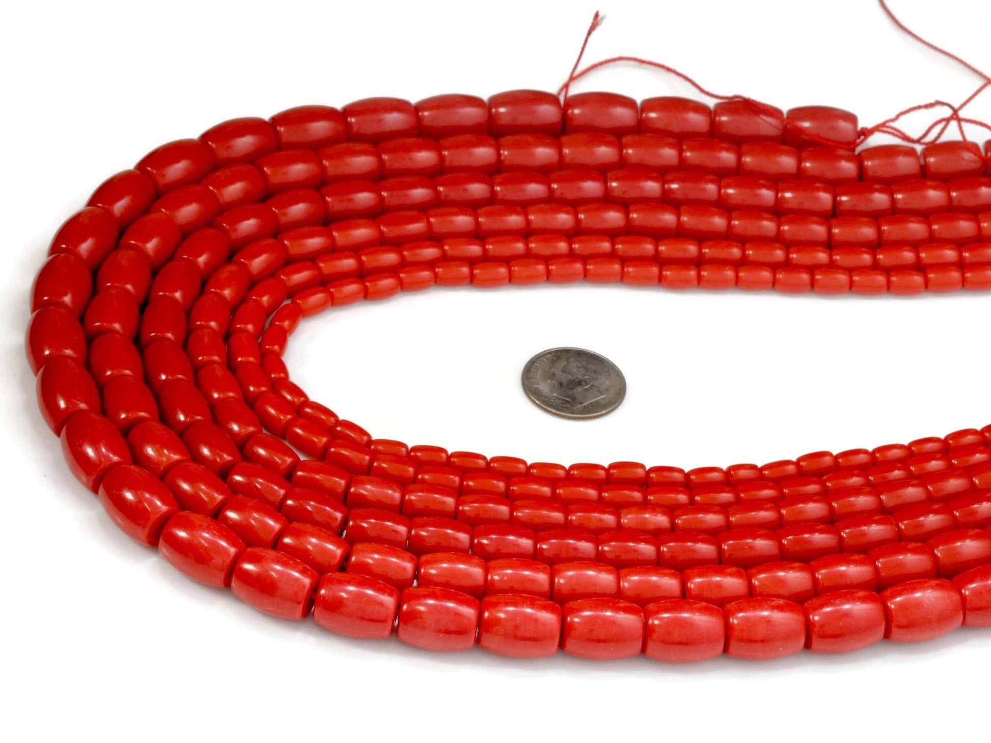 Natural coral beads strand showcasing vibrant red beads next to a coin for scale.