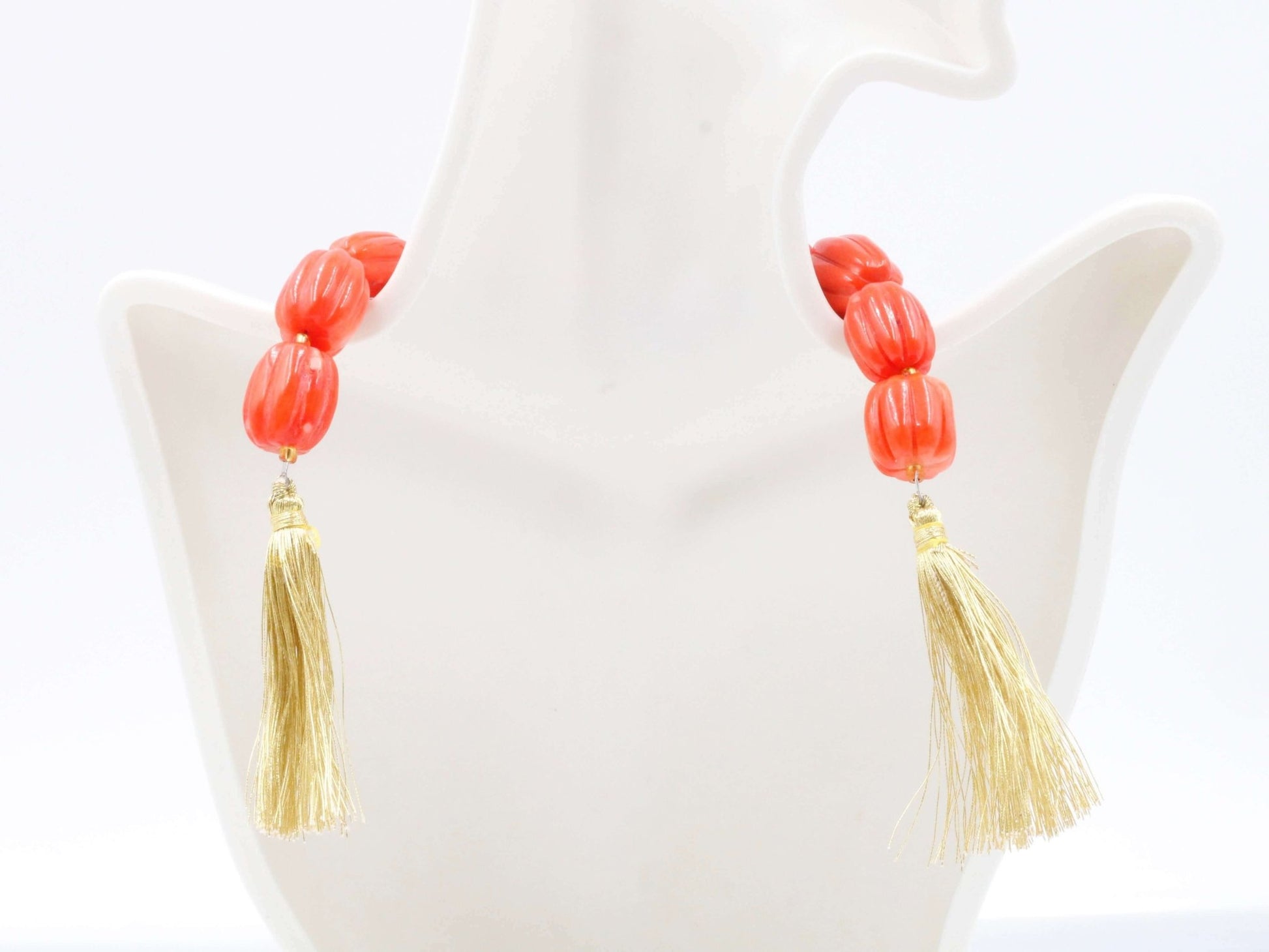 Natural orange coral beads strand with tassels displayed on a neck form.