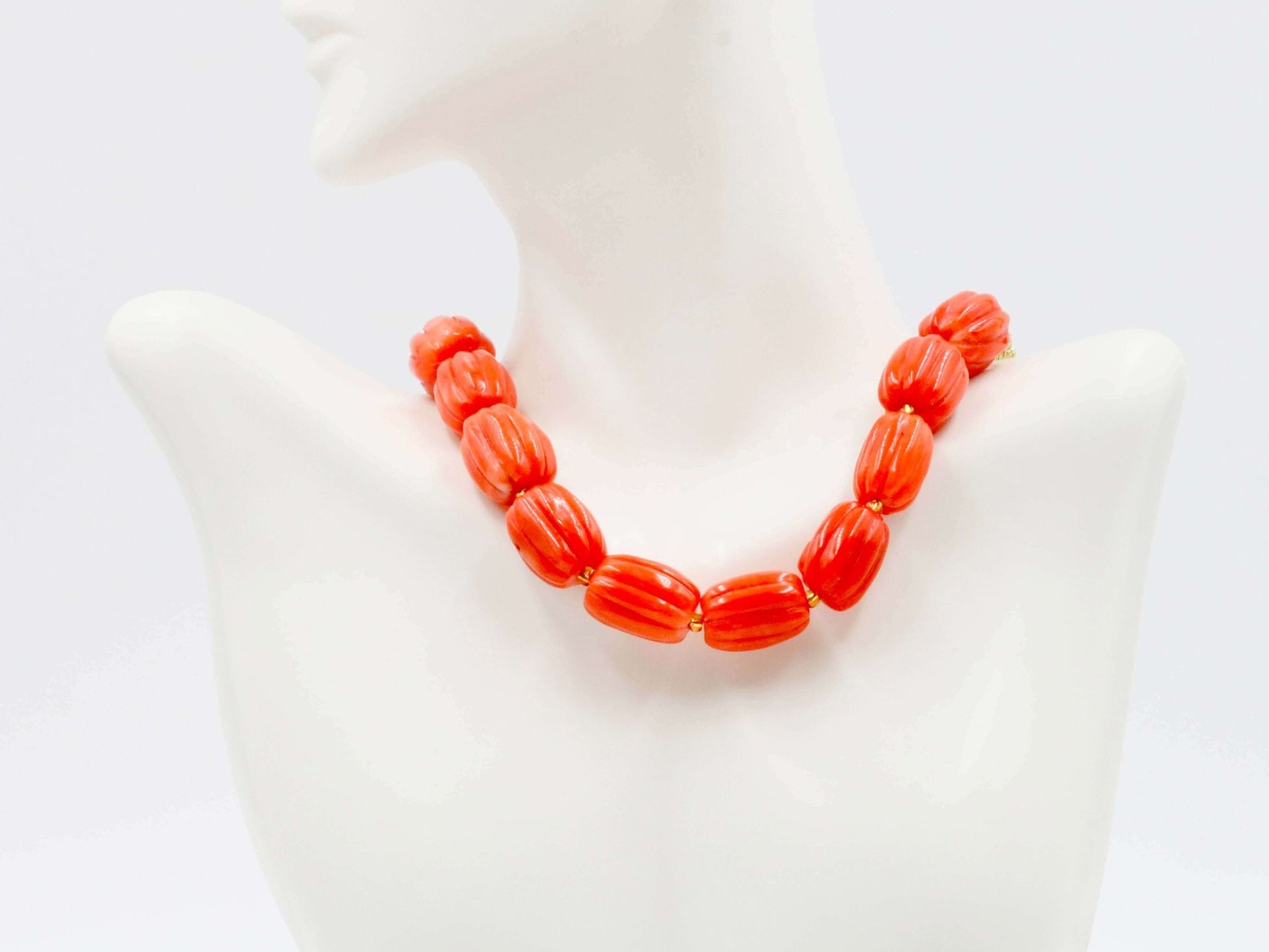 Natural orange coral beads strand showcased on a mannequin necklace display, vibrant and warm in color.