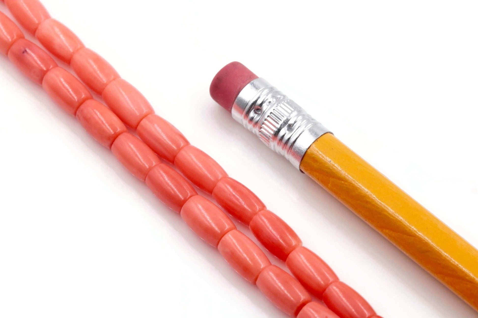 Natural orange coral beads strand next to a yellow pencil with eraser.