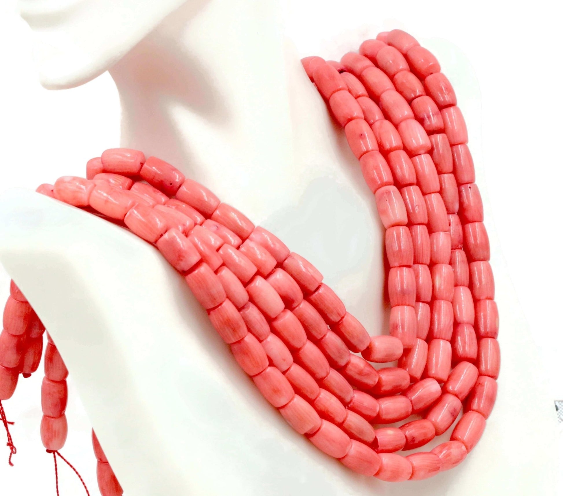 Natural pink coral beads strand displayed on a mannequin showcasing its vibrant color and barrel cut.