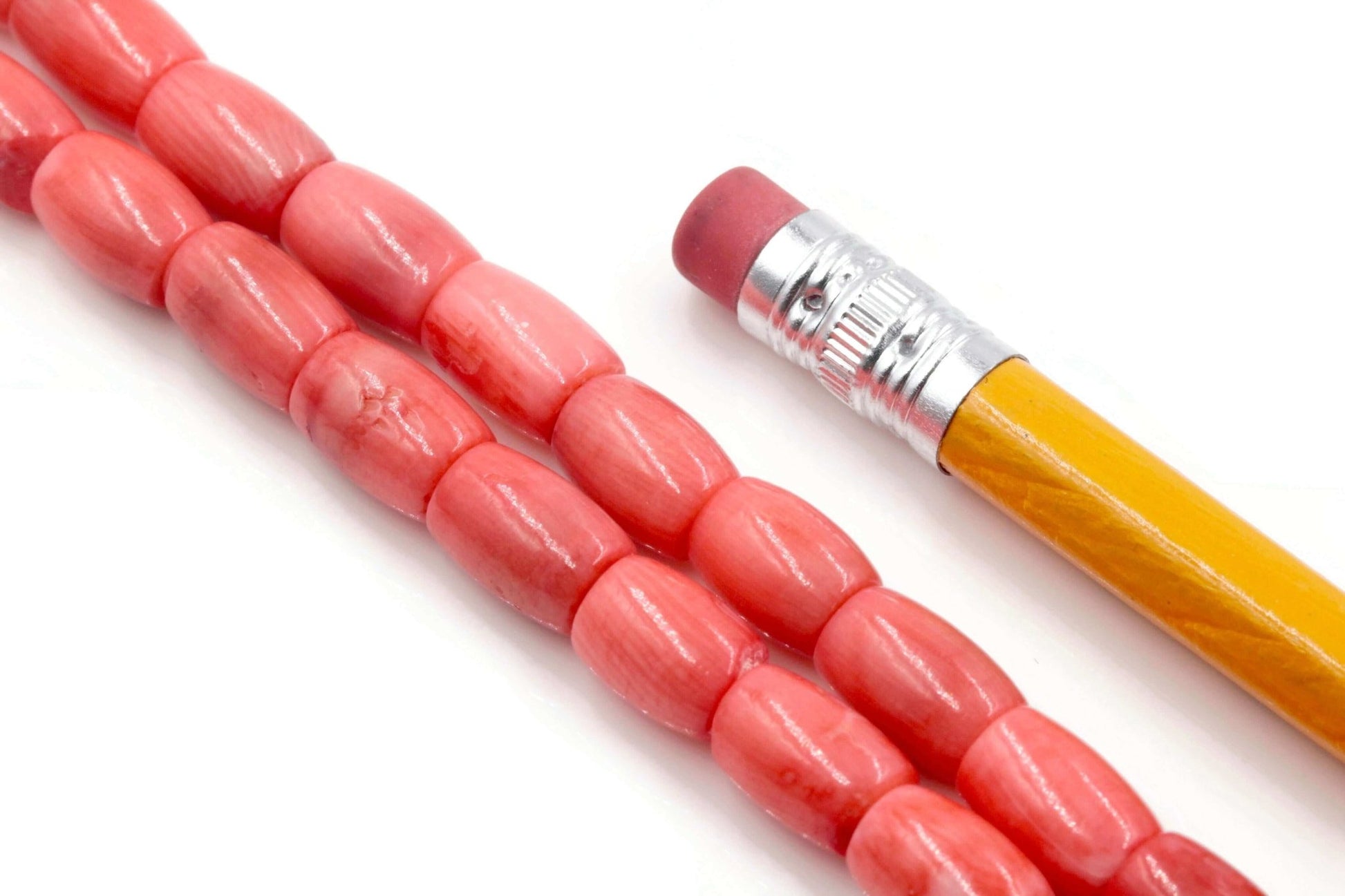 Natural pink coral beads strand displayed with a pencil for size reference, showcasing semi-translucent barrel-cut stones.