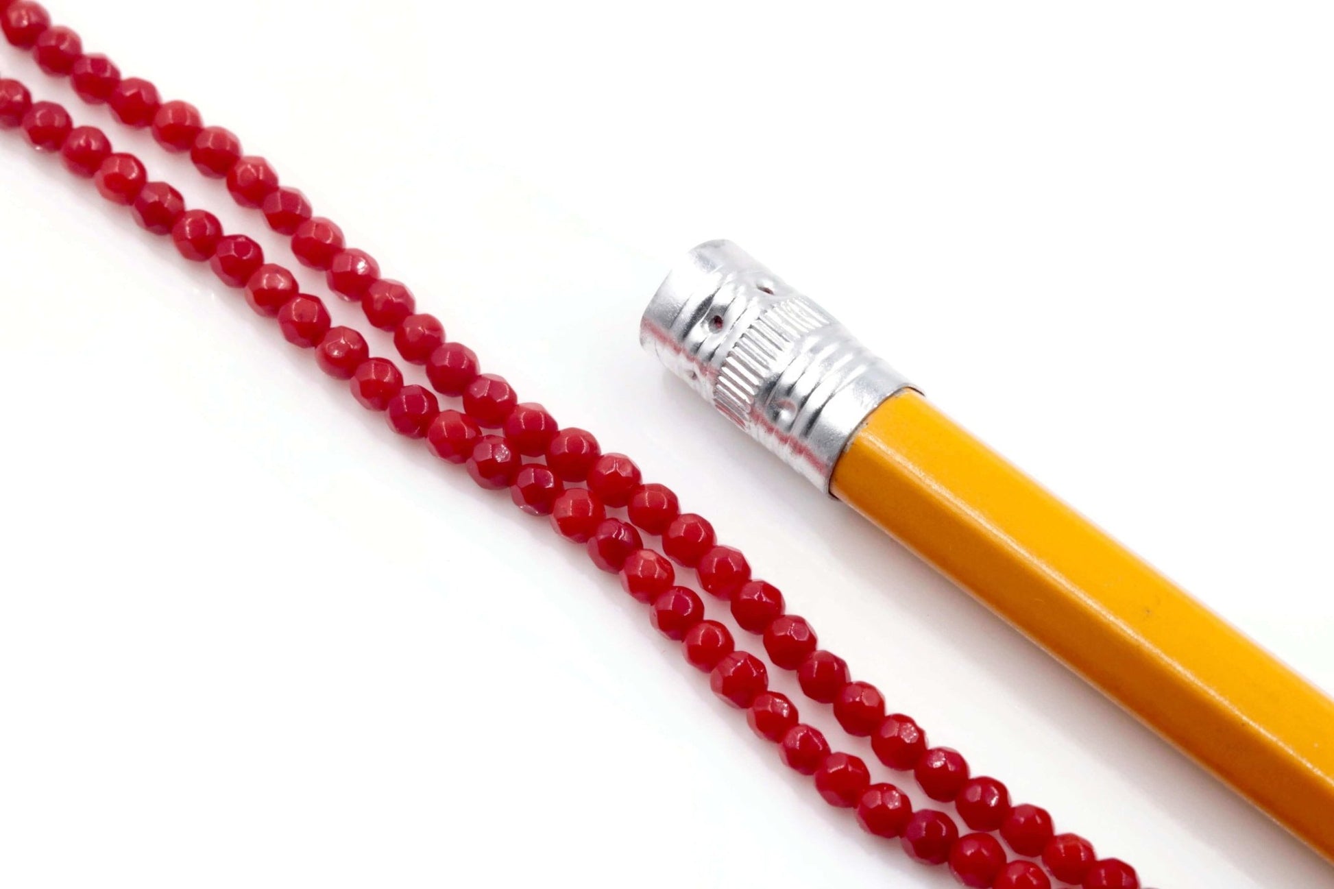 Natural red coral beads strand necklace with a pencil for scale on a white background.