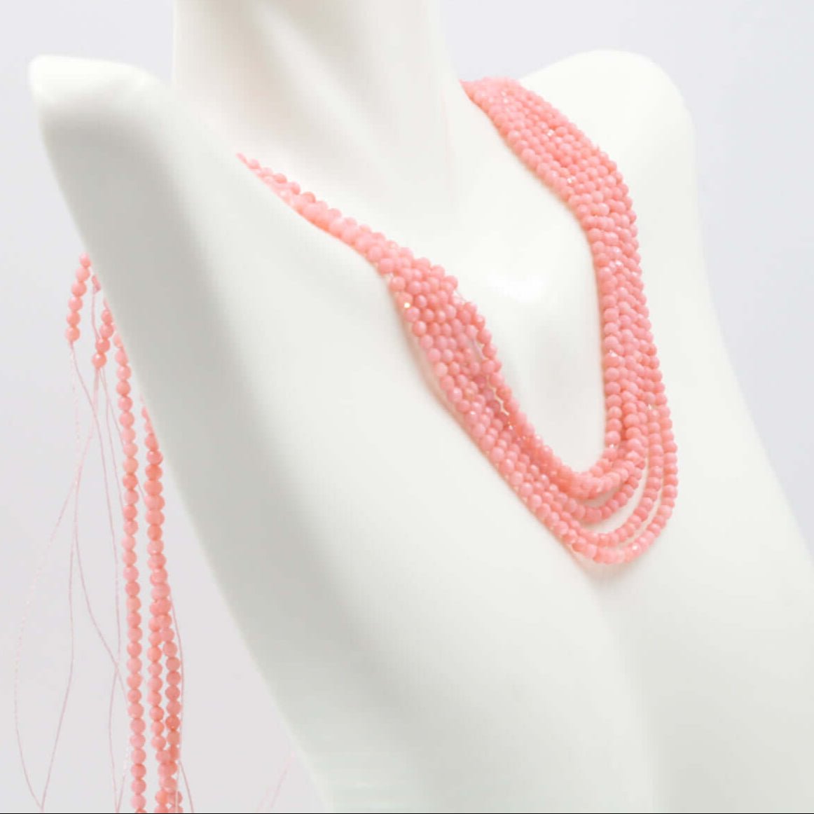 Pink coral beads strand displayed on a mannequin neck showcasing its round, opaque, faceted shape.