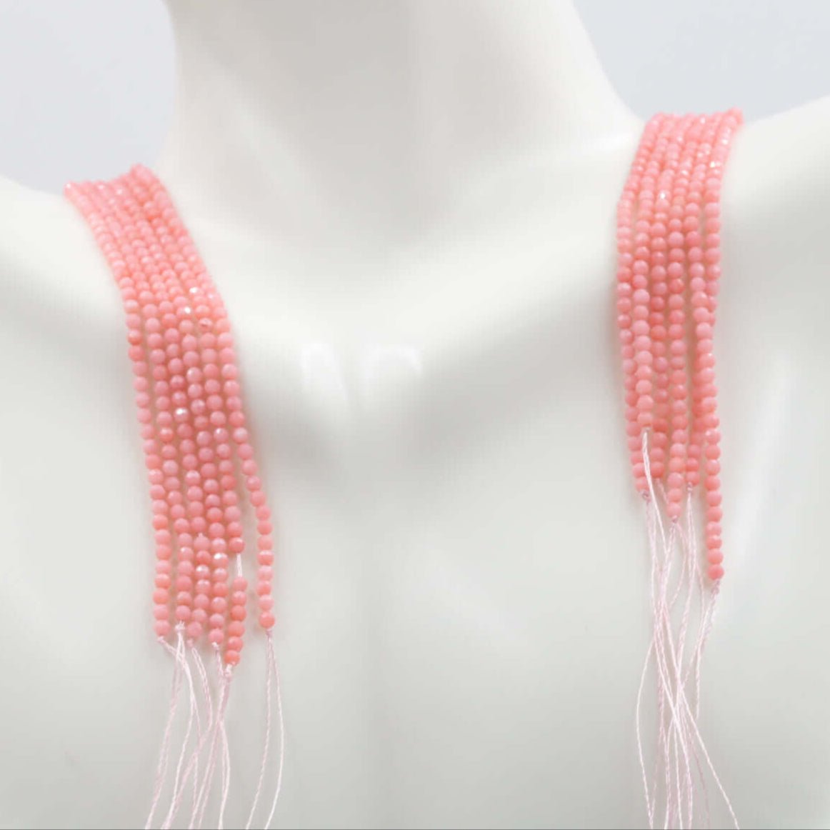Pink coral beads strand displayed on a mannequin, showcasing multiple strands of round faceted beads.