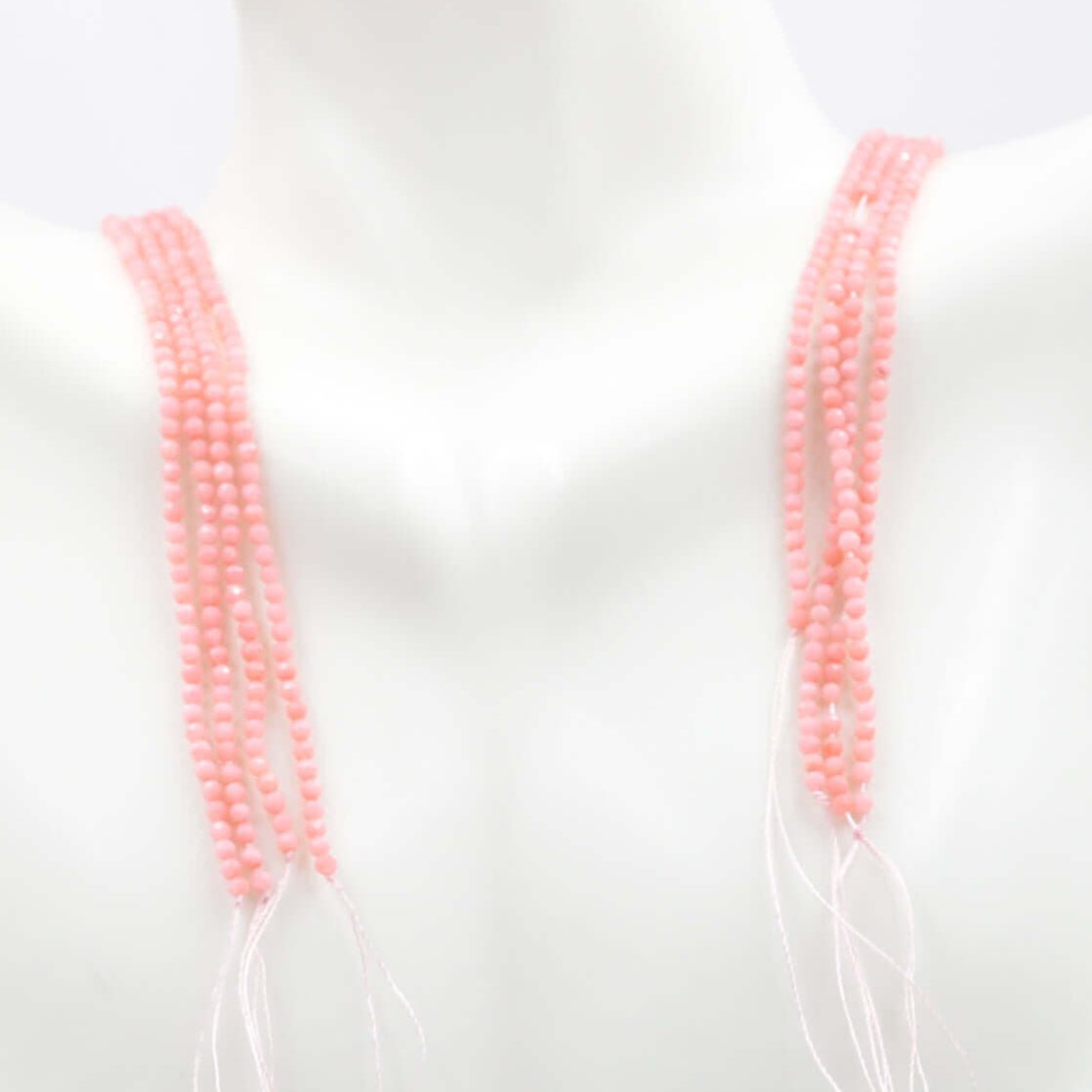 Pink coral beads strand displayed on a mannequin, showcasing unfinished beading options in opaque round faceted design.