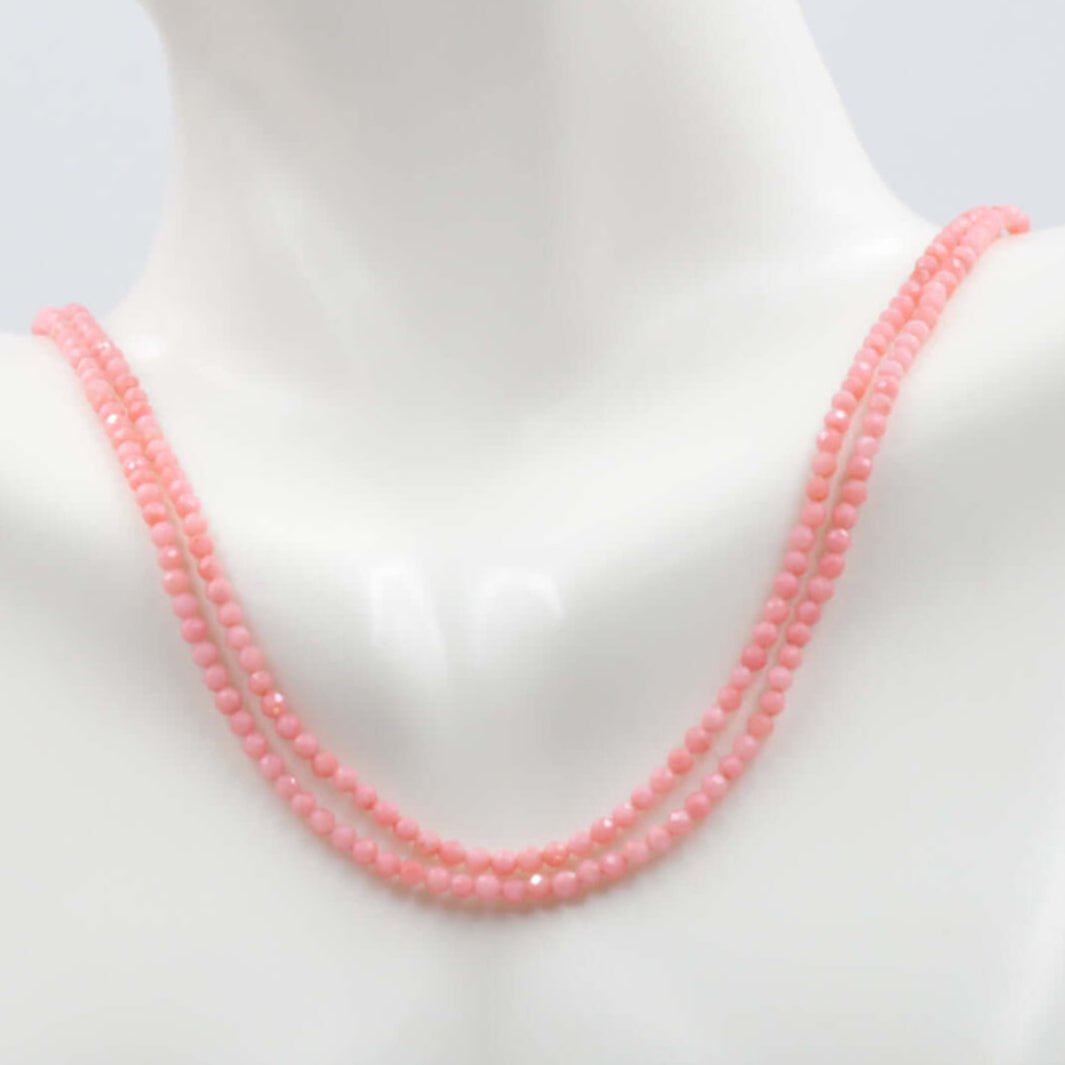 Pink coral beads strand displayed on a mannequin, showcasing the round faceted beads in a lovely pink hue.