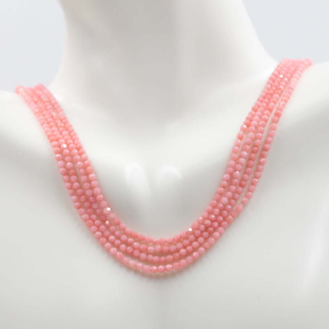 Pink coral beads strand displayed on a mannequin, showcasing multiple strands in soft pink color.