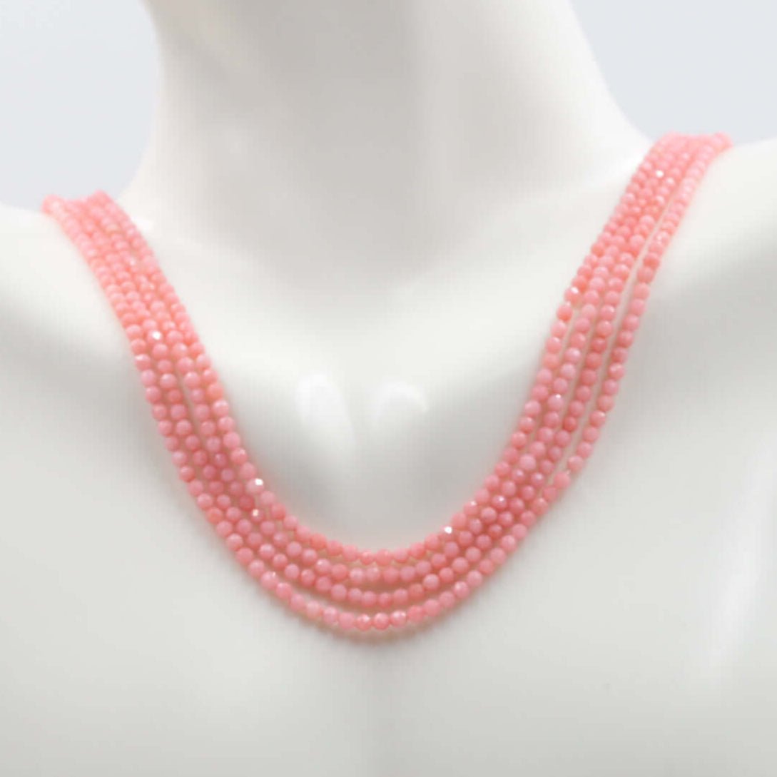 Pink coral beads strand displayed on a mannequin's neck, showcasing the round faceted beads in various strands.