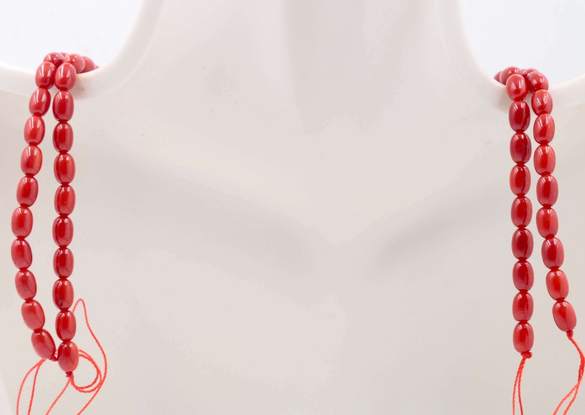 Red coral beads strand displayed on a mannequin, showcasing the vibrant red color and oval cut of natural gemstone beads.