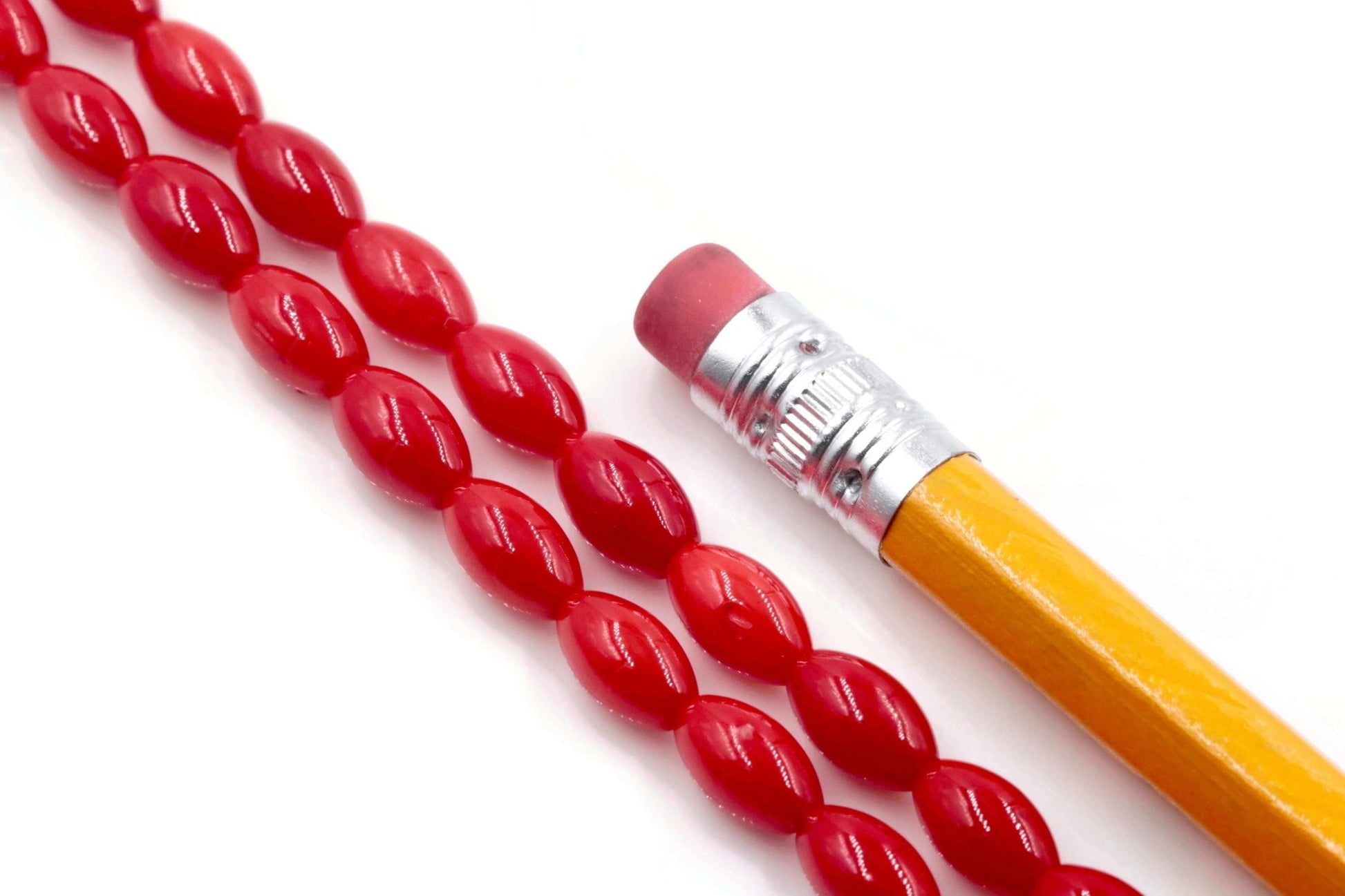 Red coral beads strand displayed next to a yellow pencil, highlighting the natural beauty of the gemstones.